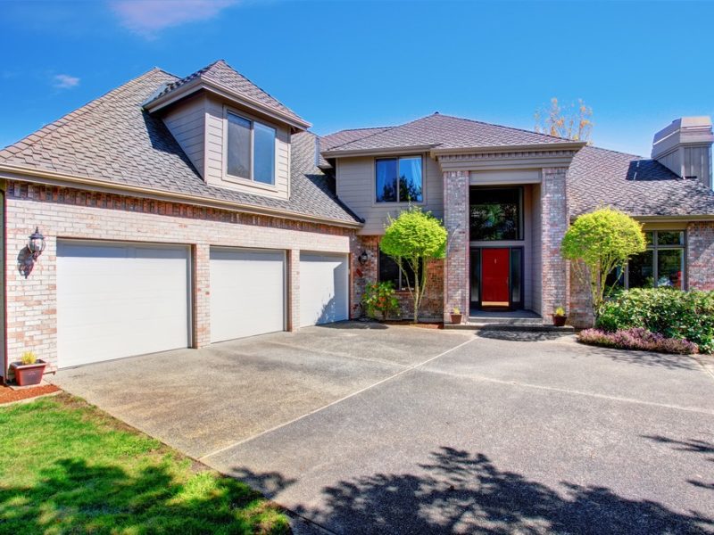 Large modern house with three garage spaces and concrete driveway. View of high ceiling porch with brick walls