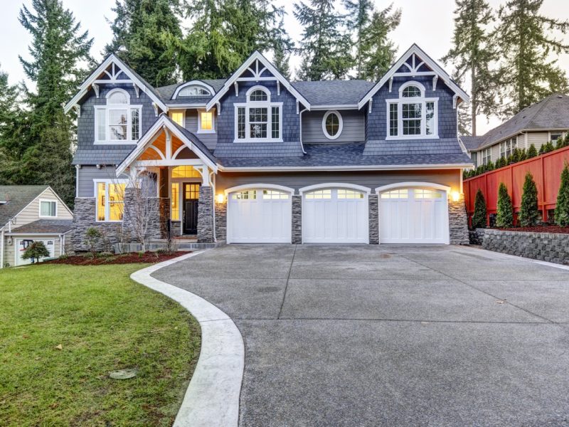 Luxurious home exterior with blue vinyl siding and white trim. Long concrete driveway lead to three attached garage spaces. Beautiful curb appeal. Northwest, USA